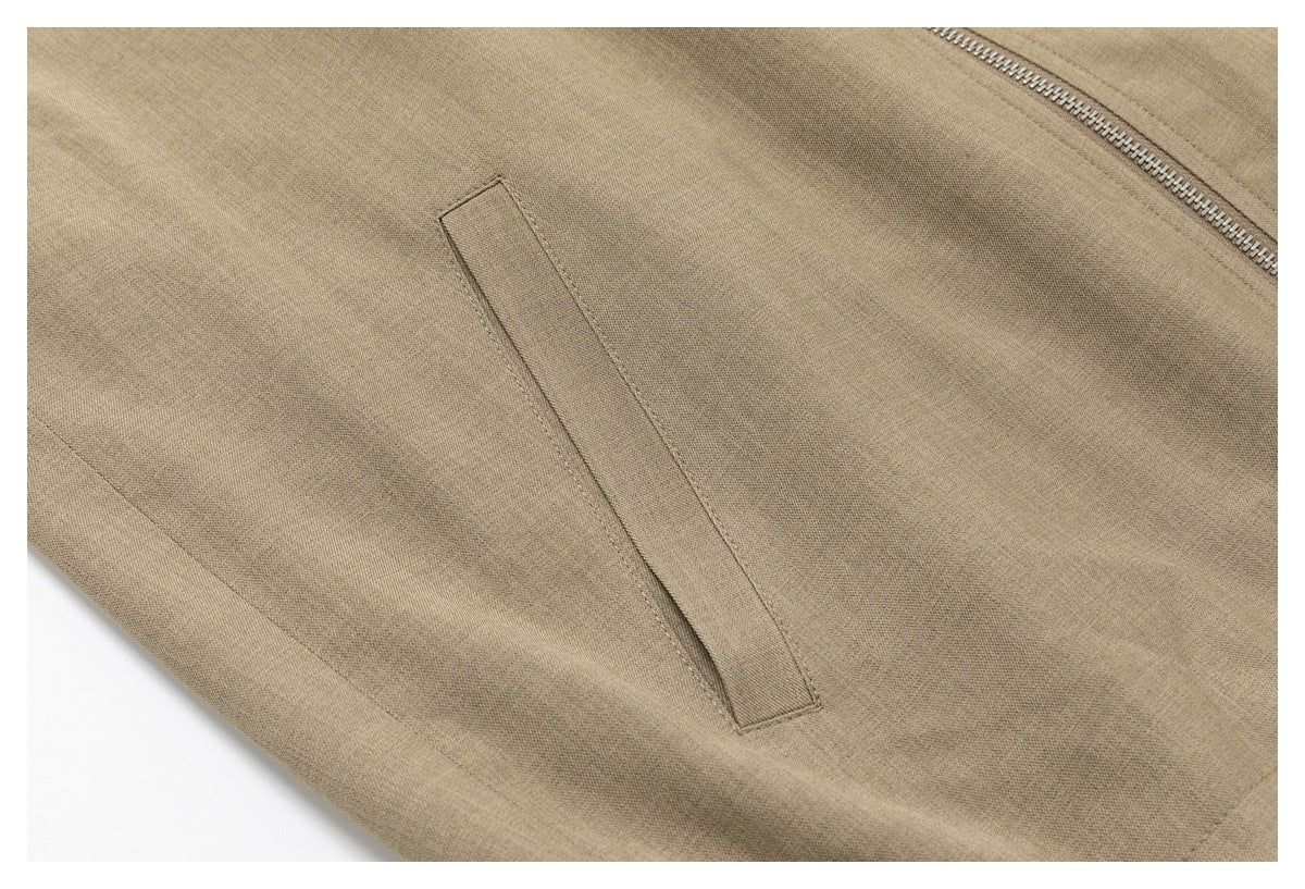 Close-up of taupe garment fabric with a slanted welt pocket and part of a metal zipper.