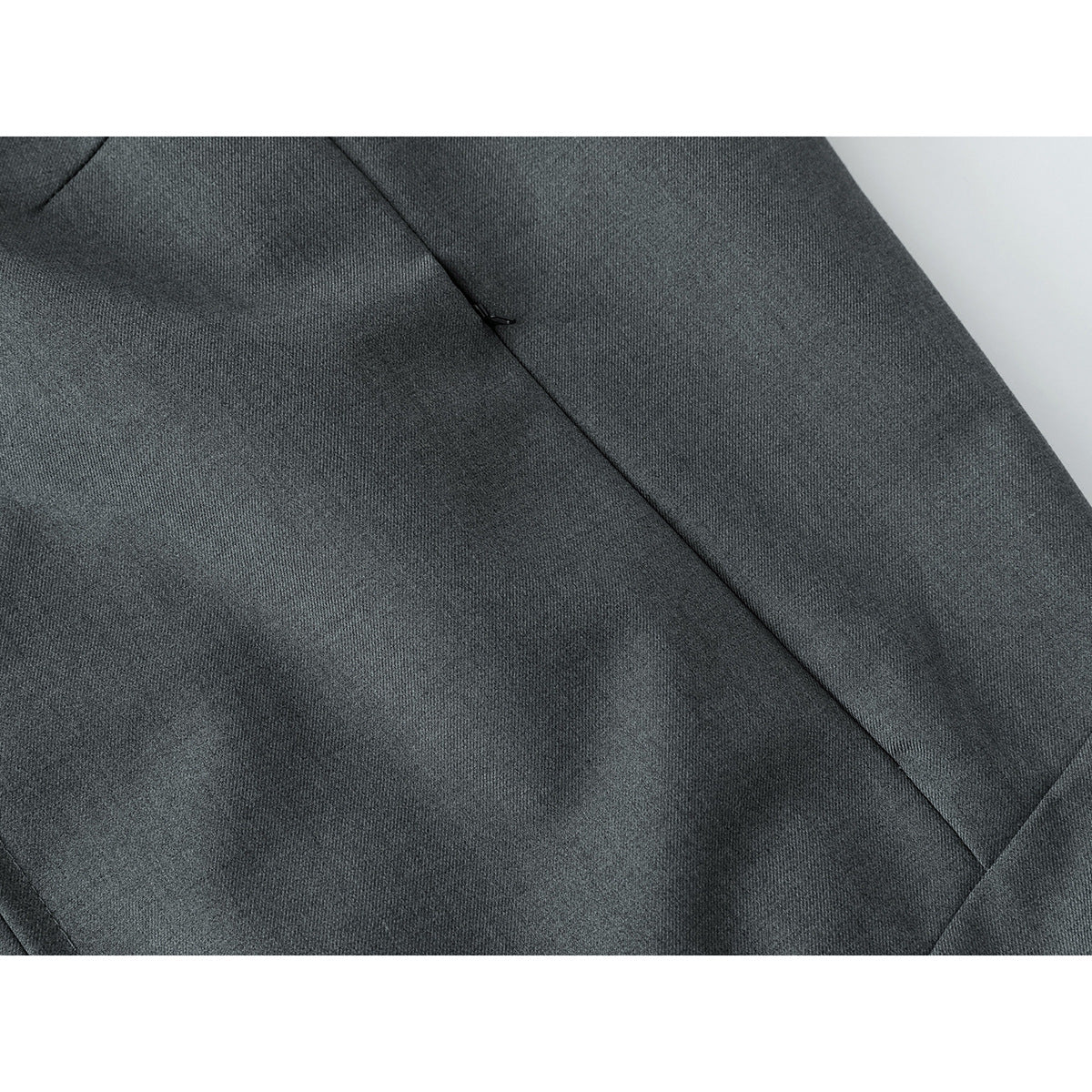 Close-up of charcoal gray jacket fabric with a diagonal seam and small pocket opening.