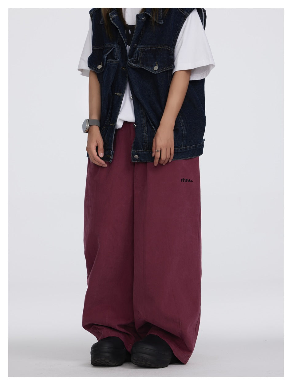 Front view of a person wearing burgundy wide-leg pants with a dark denim vest, white tee and black chunky shoes