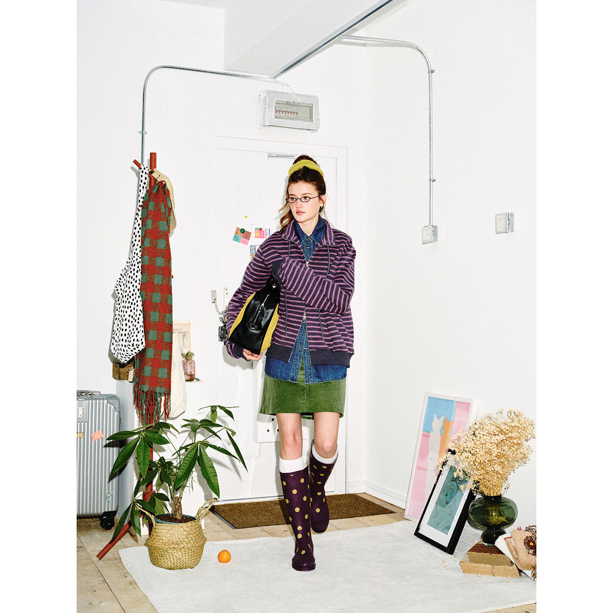 Full-length front view of a model wearing a purple striped jacket, denim shirt, green skirt and polka-dot boots.