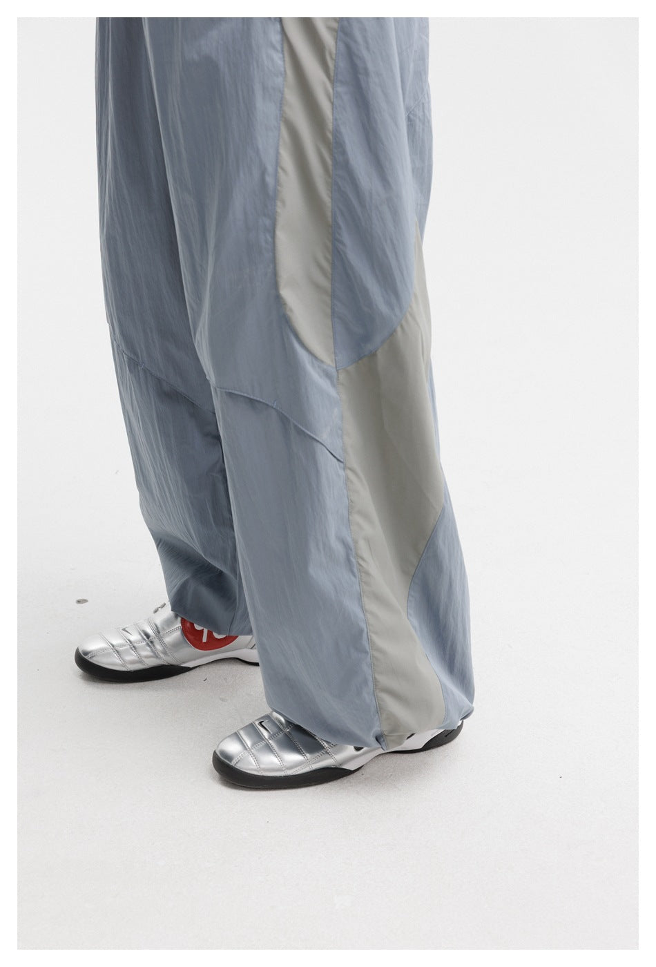 Close view of light blue-gray pants showing pale contrast side panels, curved seams, and gathered hems.