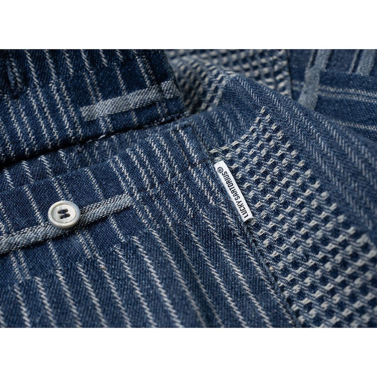 Close-up of blue patterned shirt fabric, a button, textured stitching, and a small sewn-in label.
