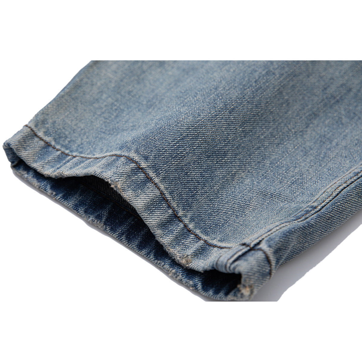Close-up of the folded hem and stitching on blue washed jeans.