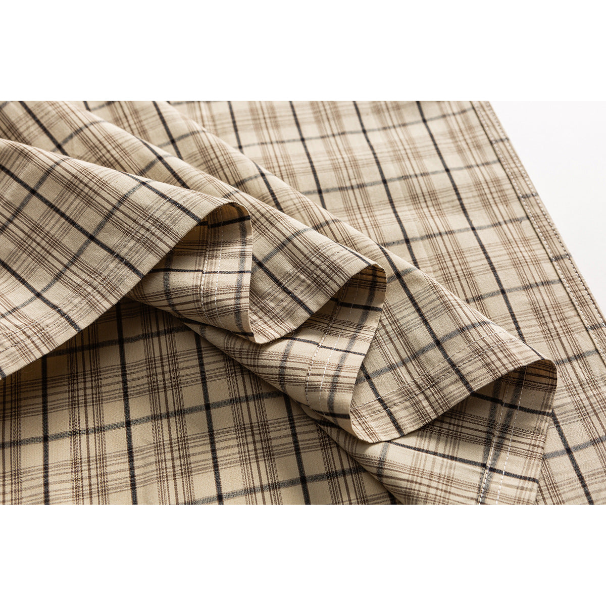 Close-up of beige plaid shirt fabric folded to show its stitched hem and pattern.