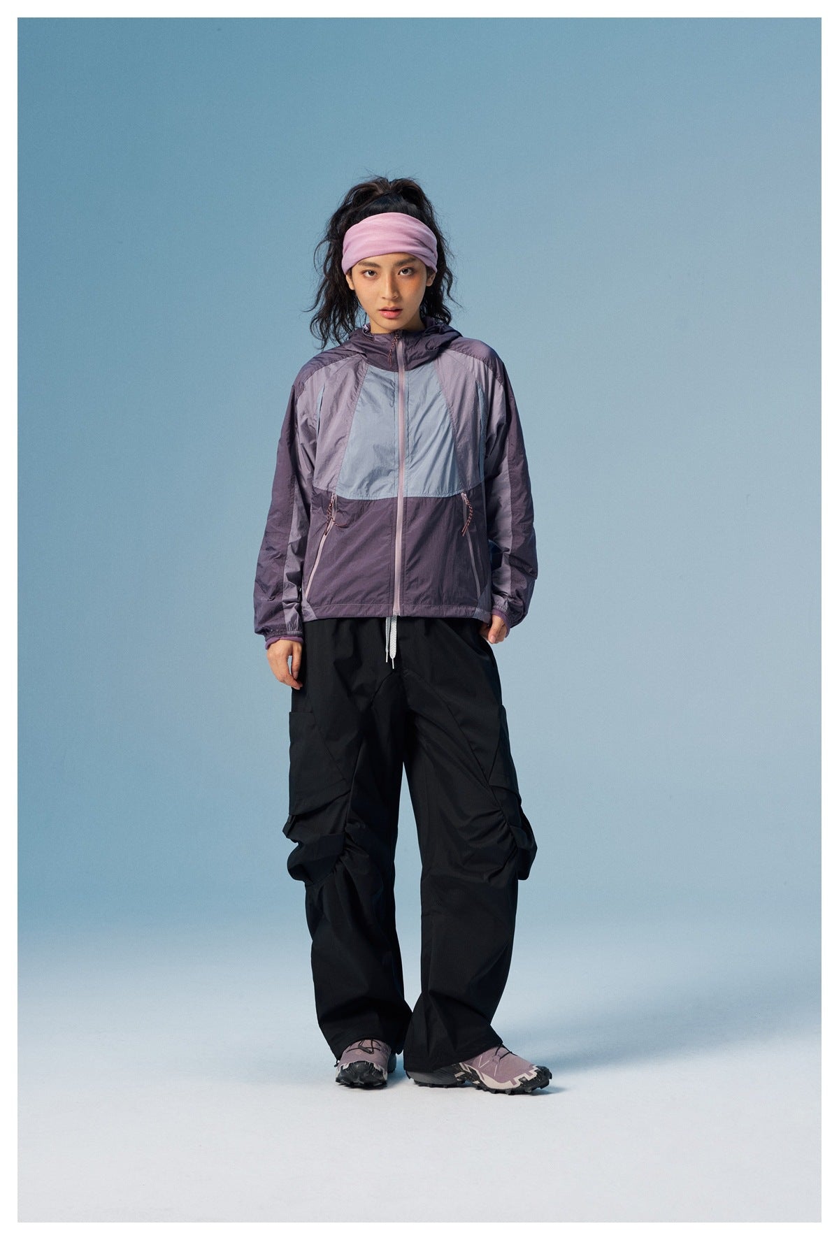 Model wearing a purple color-block hooded jacket with black cargo pants and a pink headband.