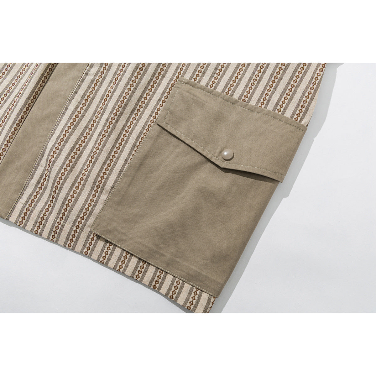 Close-up of a large taupe flap pocket with a snap on the beige striped shirt.
