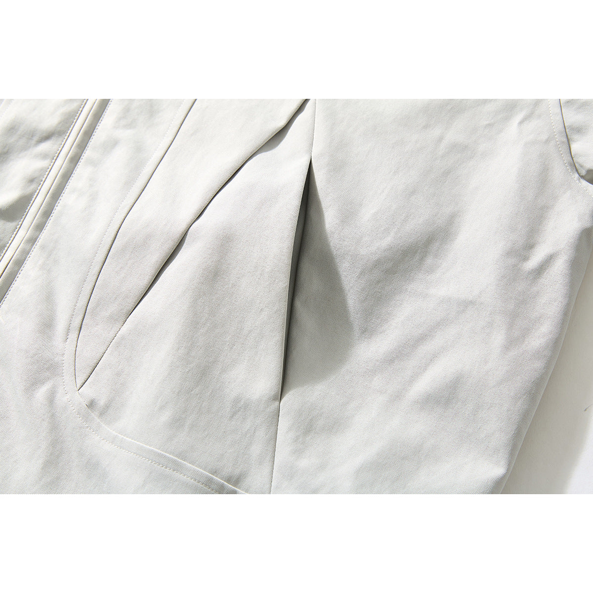 Close-up of an off-white jacket's curved front pocket and stitched panel seams.