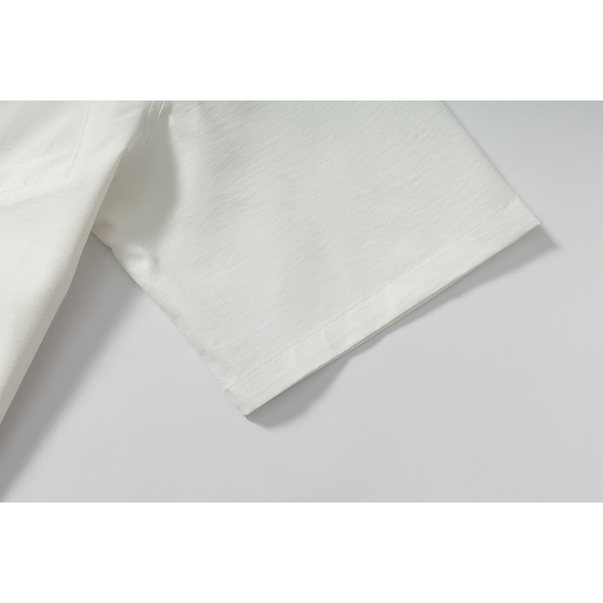 Close-up of the short sleeve and stitched hem of an off-white shirt.
