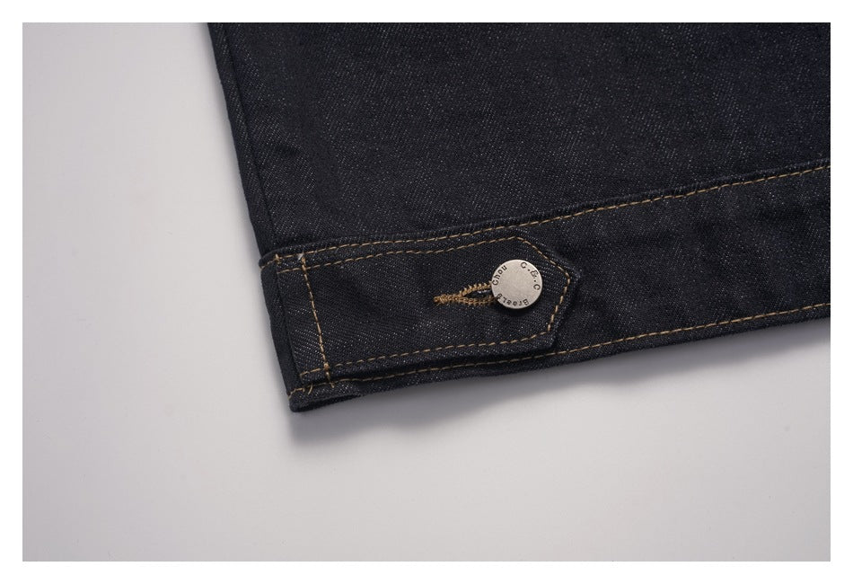 Close-up of dark denim hem with tan contrast stitching and a small silver button.