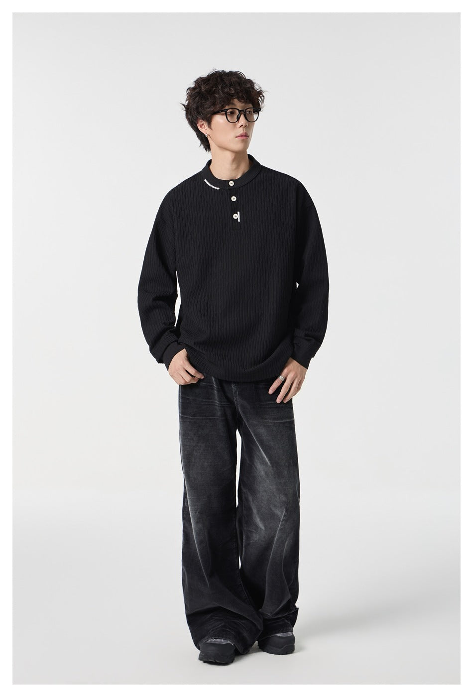 Model wearing a black ribbed Henley with a short button placket and dark wide-leg trousers.