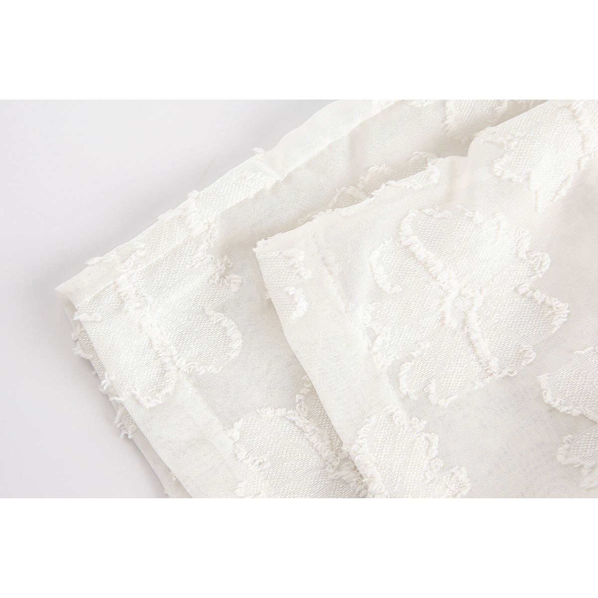 Close-up of white raised floral-textured fabric and folded garment edges.