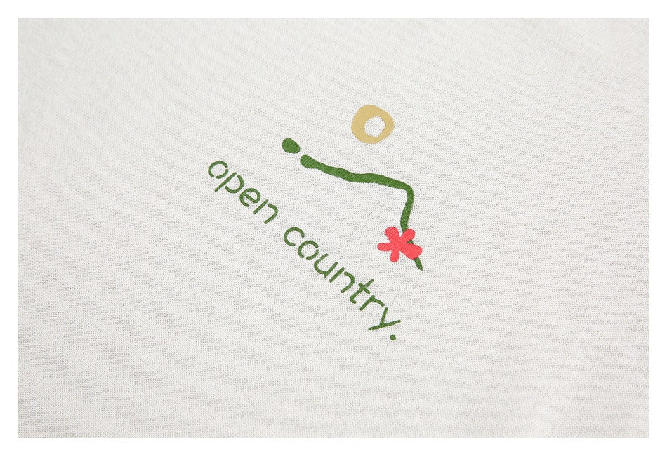 Close-up of a green “open country” graphic with a red flower on off-white fabric.