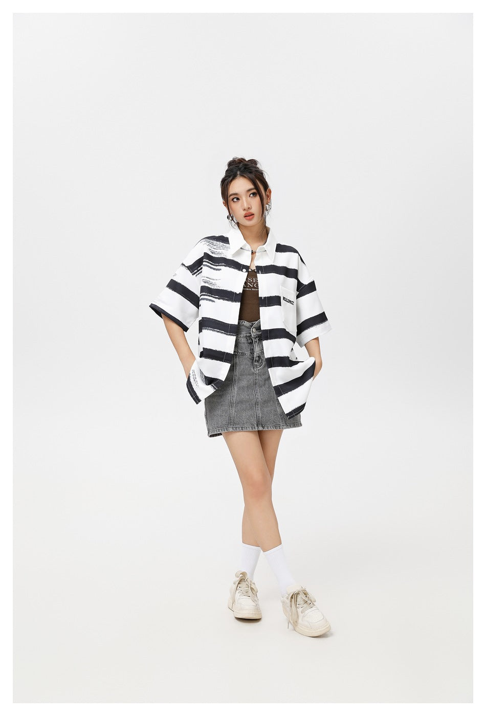 Model wearing an oversized white short-sleeve shirt with bold black brushstroke stripes, layered over a dark top and gray