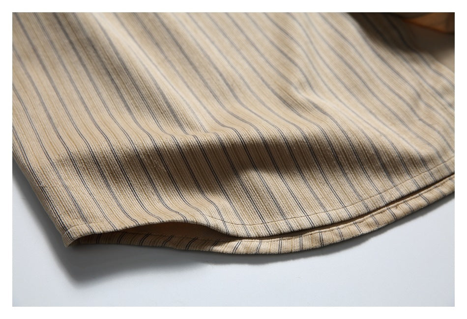 Close-up of the curved stitched hem on a beige shirt with fine dark vertical stripes.