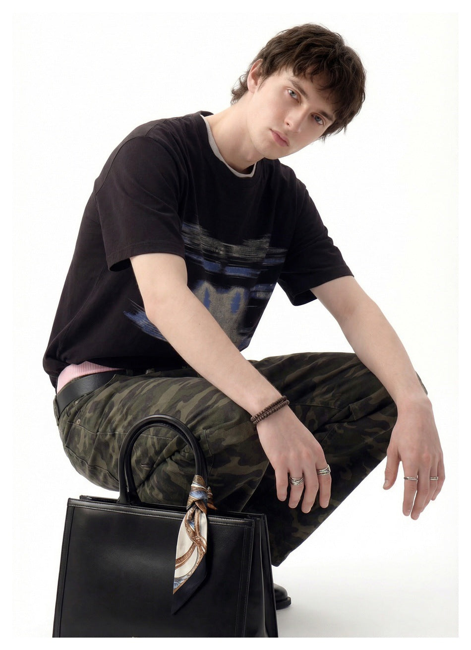 Model crouching in a black short-sleeve T-shirt with an abstract blue-gray chest graphic.