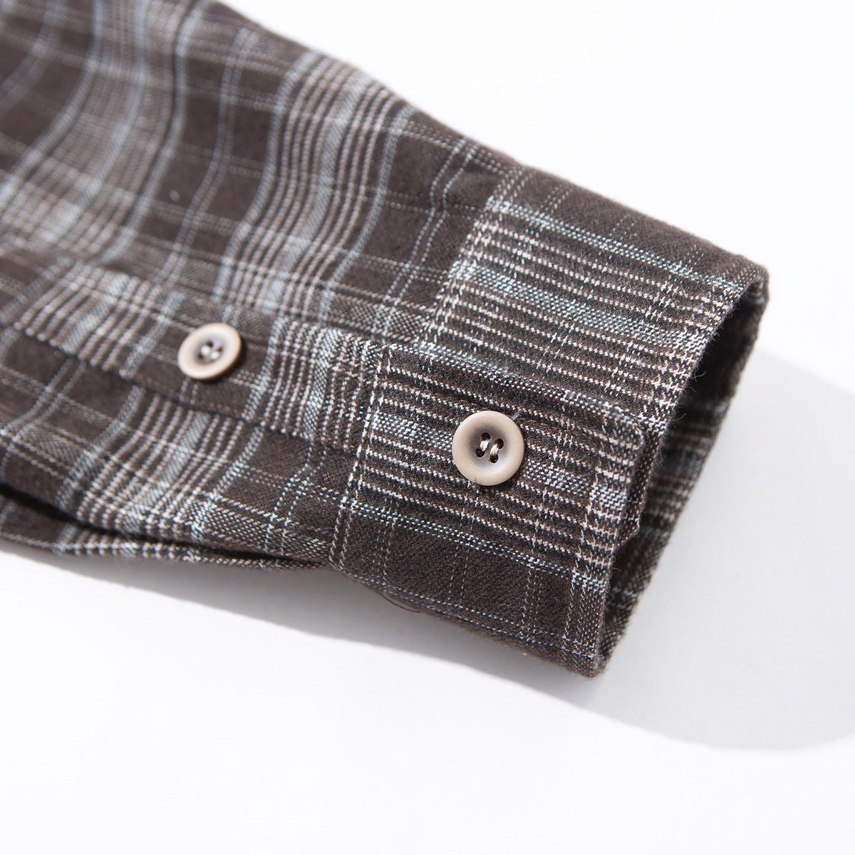 Close-up of a brown and gray plaid shirt cuff with a button and matching patterned sleeve.