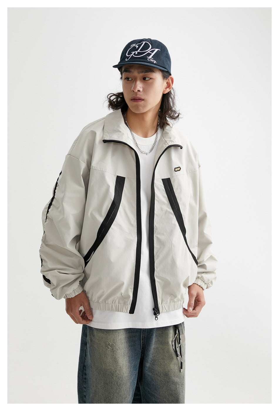 Front view of a model in a light gray jacket with black piping, curved pocket trim, and elastic cuffs and hem.