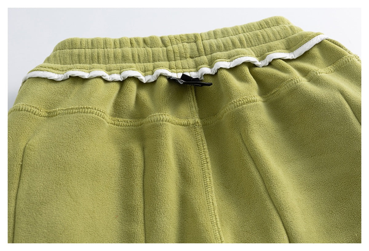 Close-up of olive-green garment waistband with elastic gathers, white wavy trim, and visible stitching.