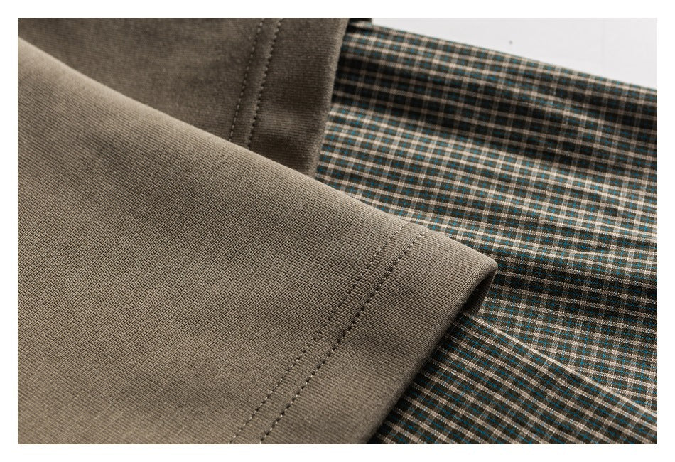 Close-up of a taupe sleeve hem and stitching beside green, brown, and cream plaid fabric.