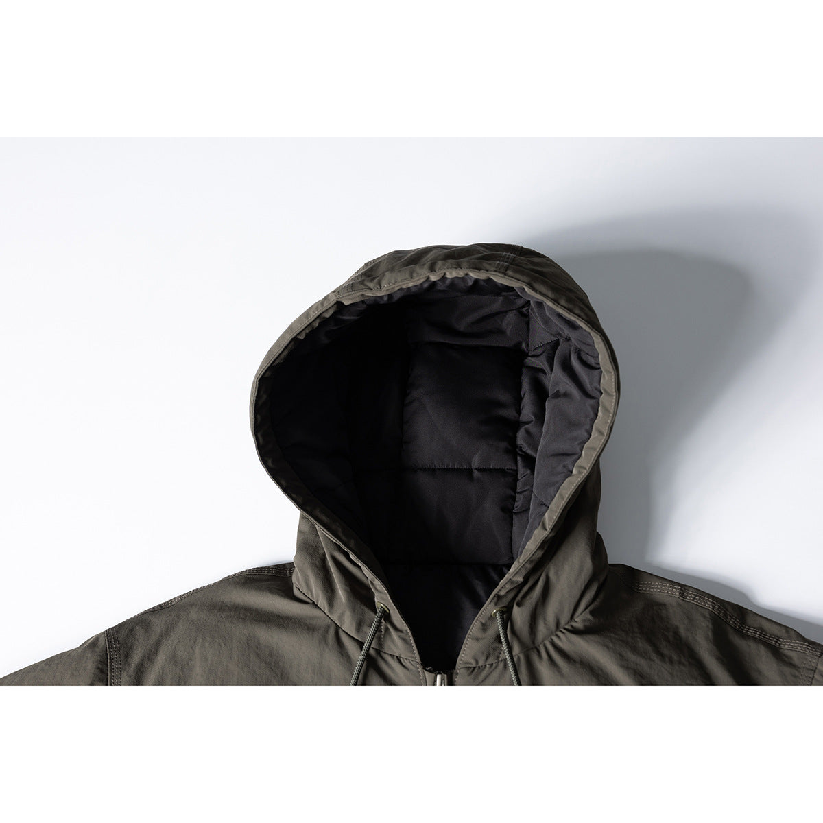 Close-up of an olive-gray hooded jacket showing its black padded hood lining and drawstrings.