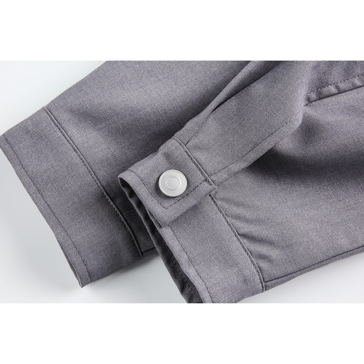 Close-up of a gray jacket cuff with a round silver snap and visible stitching.