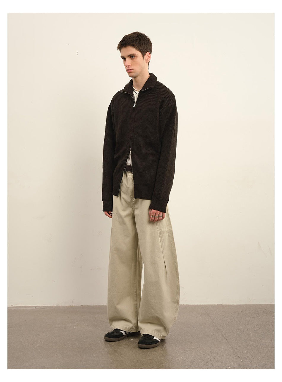 Full-length view of a man in a dark brown rib-knit zip cardigan, beige wide-leg pants and black sneakers