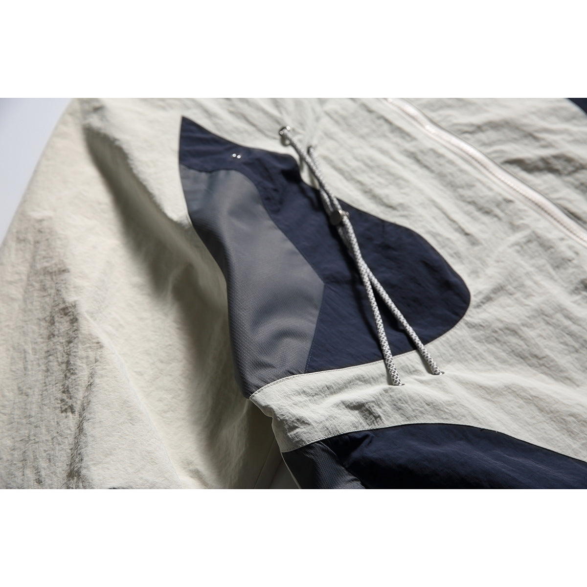Close-up of a jacket's navy and gray front pocket panel with dangling drawcords.