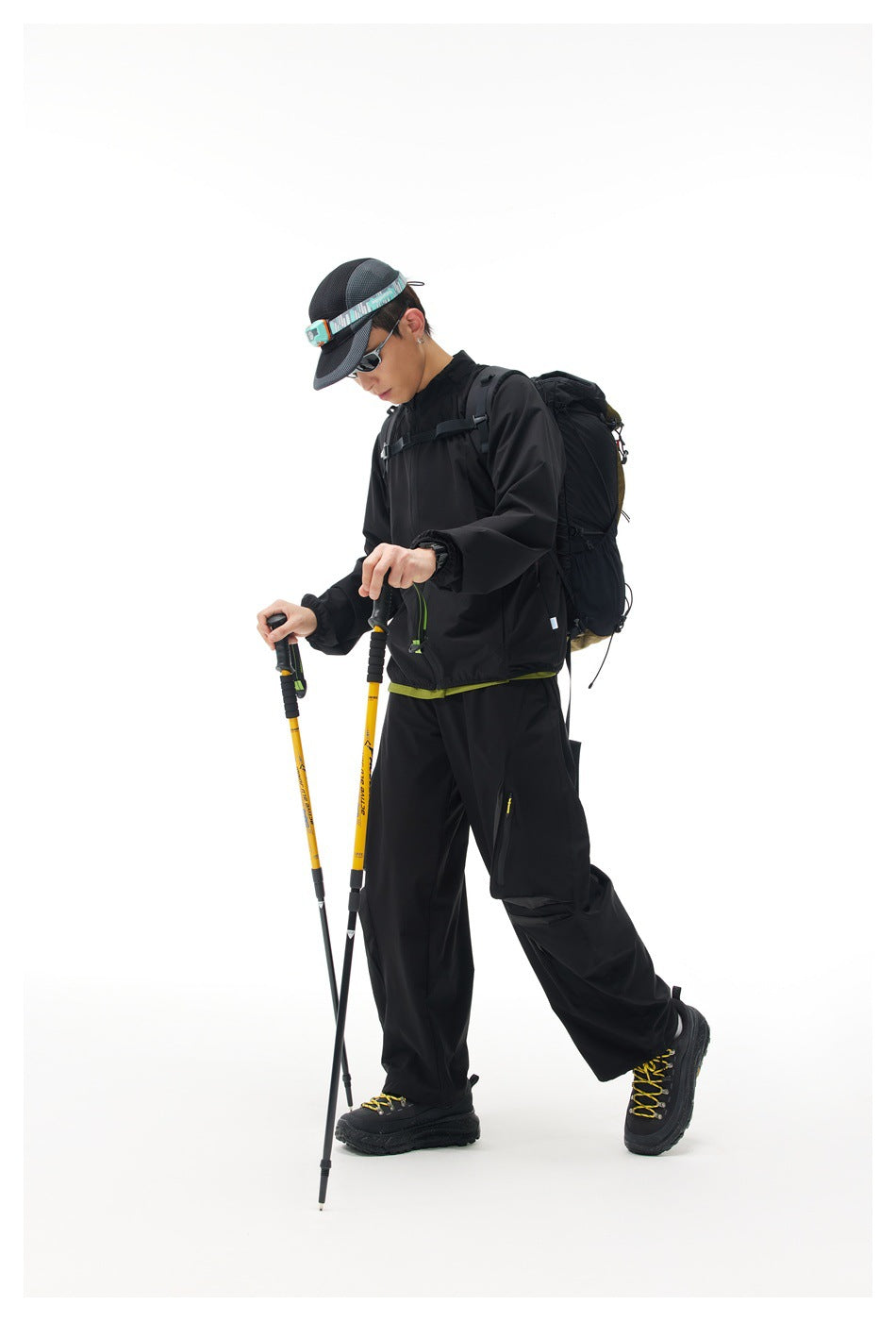 Side view of a model wearing a black hiking jacket and cargo pants with a backpack and trekking poles.