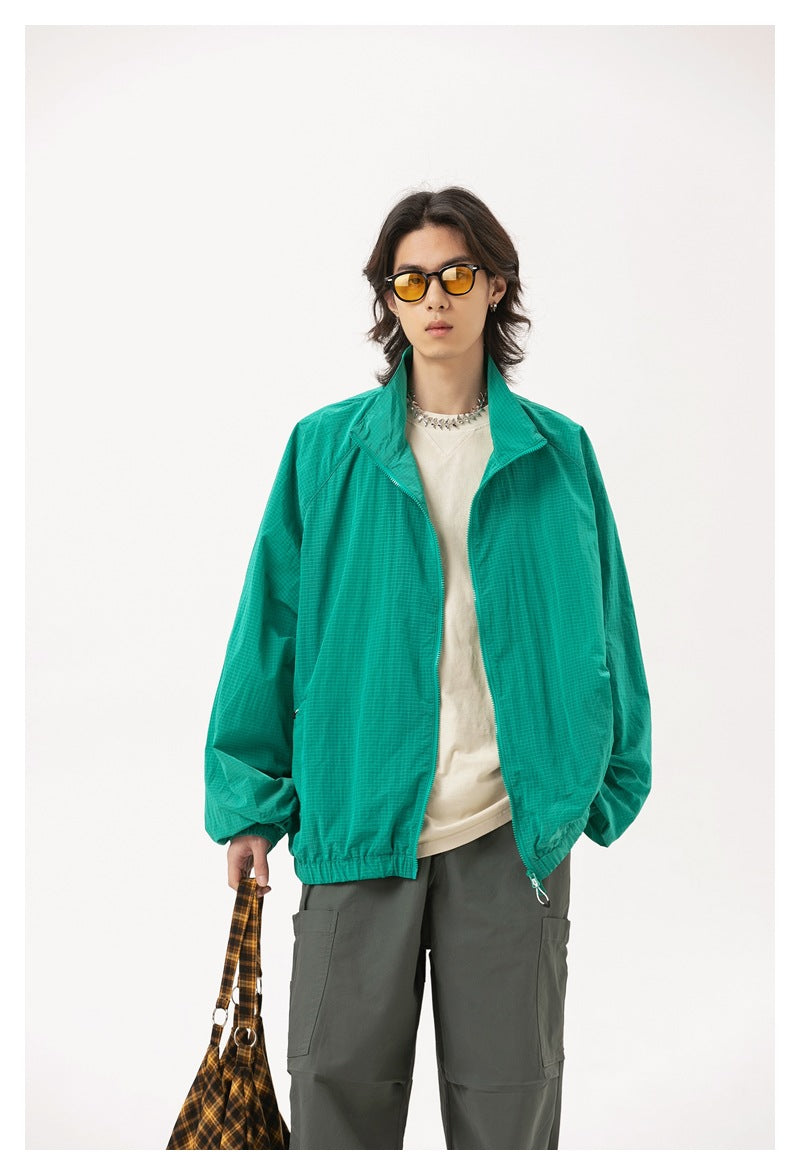 Model wearing a bright teal zip-front jacket with a raised collar and elastic cuffs, styled with gray cargo pants.