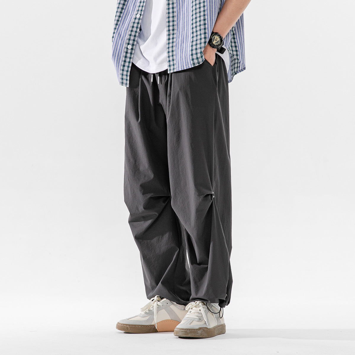 Cropped view of a model wearing loose charcoal-gray drawstring trousers with gathered ankle cuffs.