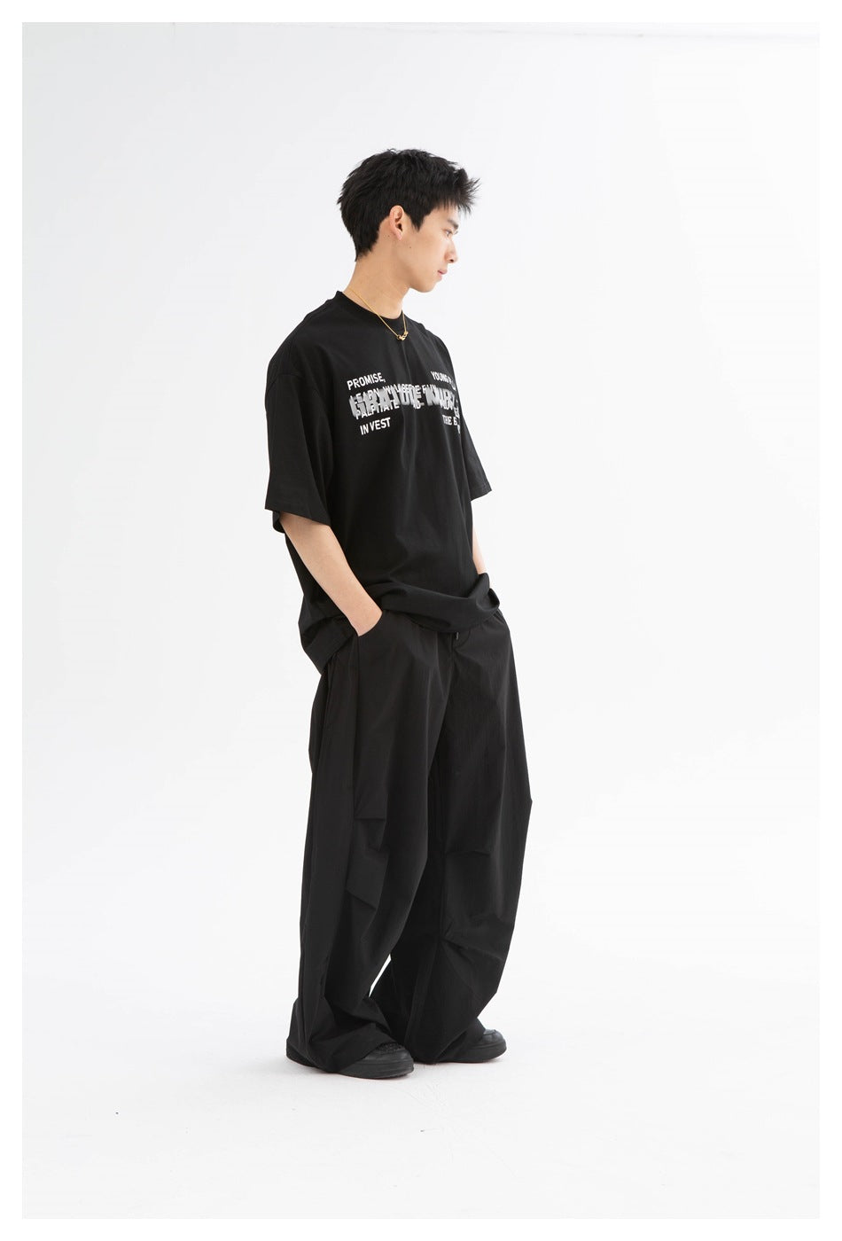Model in a black oversized graphic t-shirt and black wide-leg pants, side view with head turned down