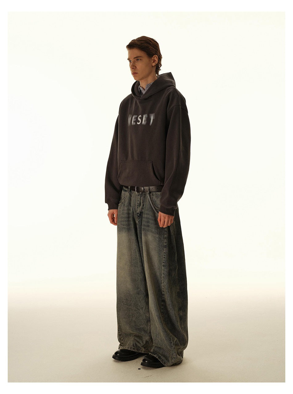 Three-quarter view of a model wearing a dark charcoal hoodie with blurred light chest lettering and oversized gray jeans.