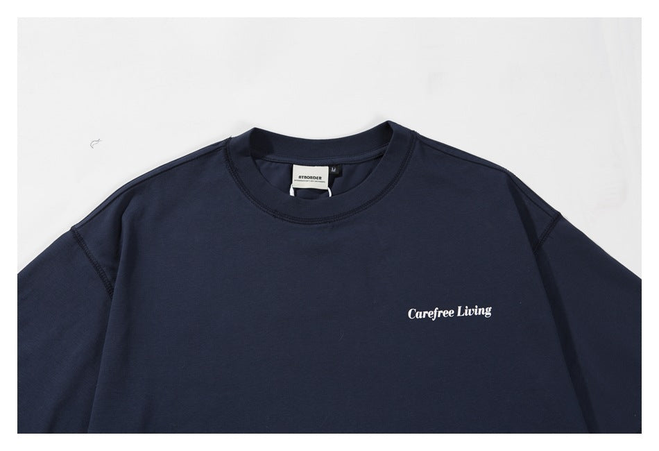 Close-up of the navy T-shirt front, showing the crew neck, stitching, and white “Carefree Living” chest print.