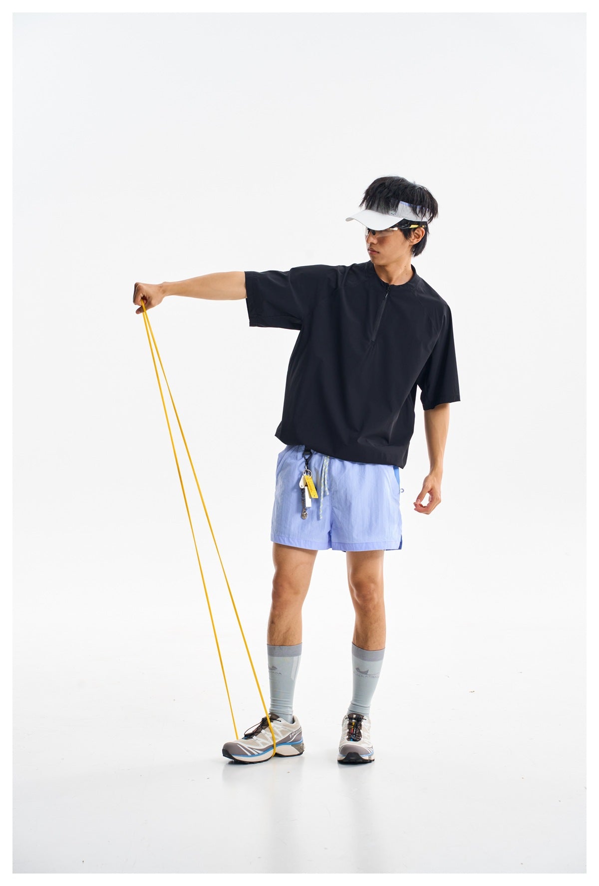 A man wears a black short-sleeve zip-neck top and light blue shorts while holding a yellow resistance band.