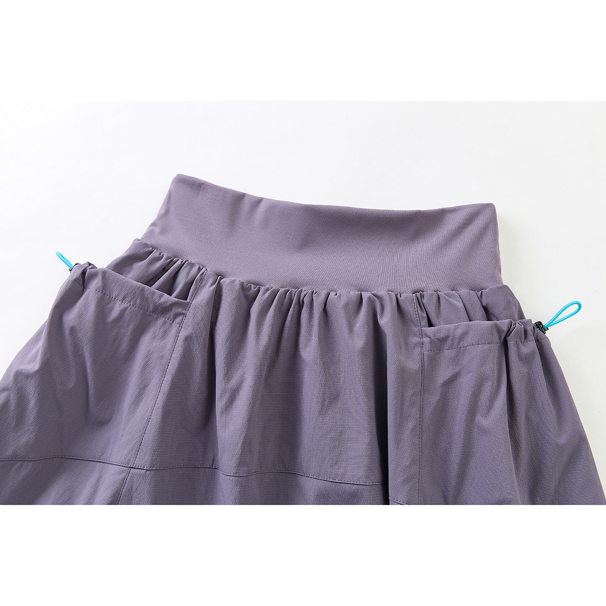 Close-up of a muted lavender skirt waistband, gathered fabric, pockets, and turquoise cord loops.
