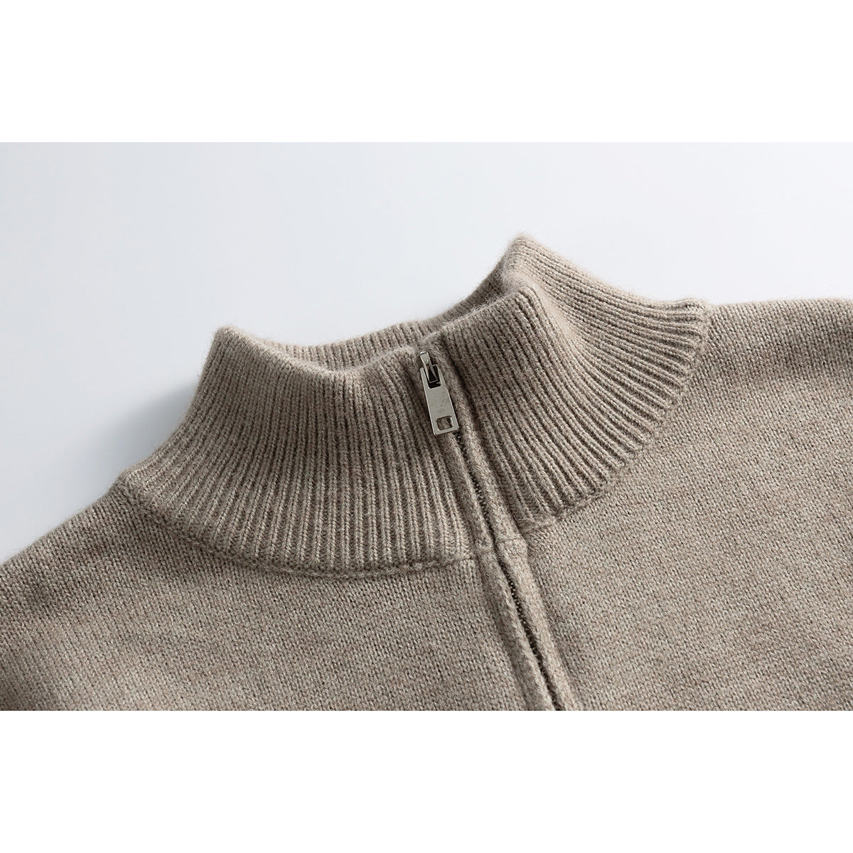 Close-up of a taupe knit sweater’s ribbed stand collar and short metal zipper.