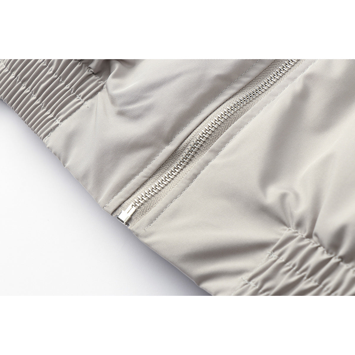 Close-up of a light gray jacket’s metal zipper and gathered elastic sleeve cuff.