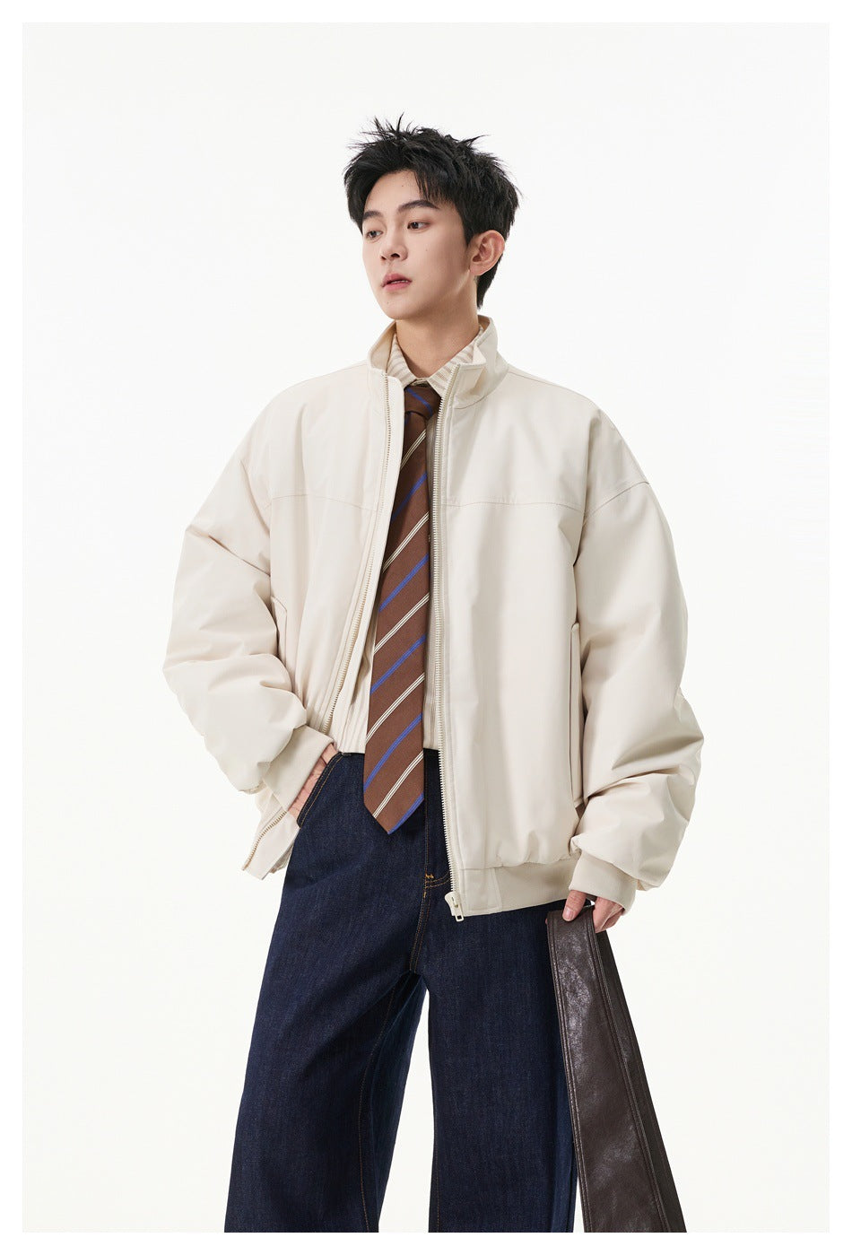 Model wearing a cream stand-collar zip jacket open over a striped shirt and tie, with dark jeans.