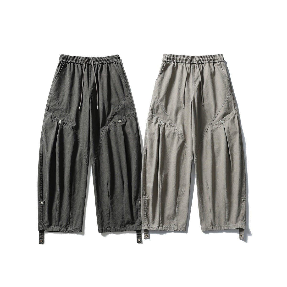 Two pairs of loose-fit pants shown from the front in charcoal and light gray, with drawstrings and snap pockets.