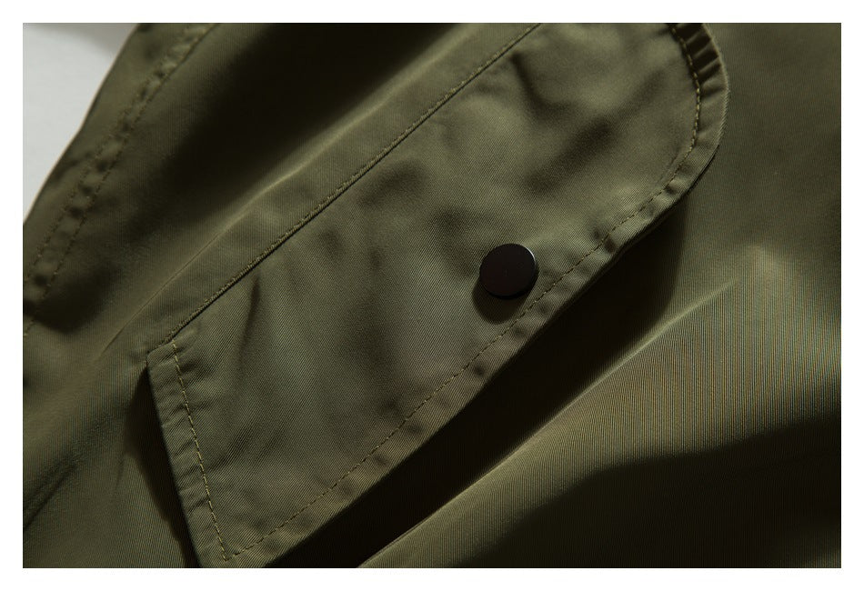 Close-up of an olive jacket pocket flap with a black snap fastener and visible stitching.