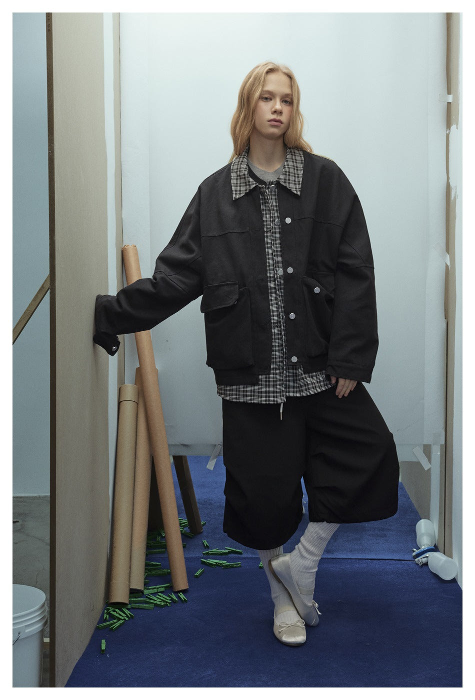 Model wearing a black oversized jacket with a black-and-gray plaid collar and placket, paired with black shorts.
