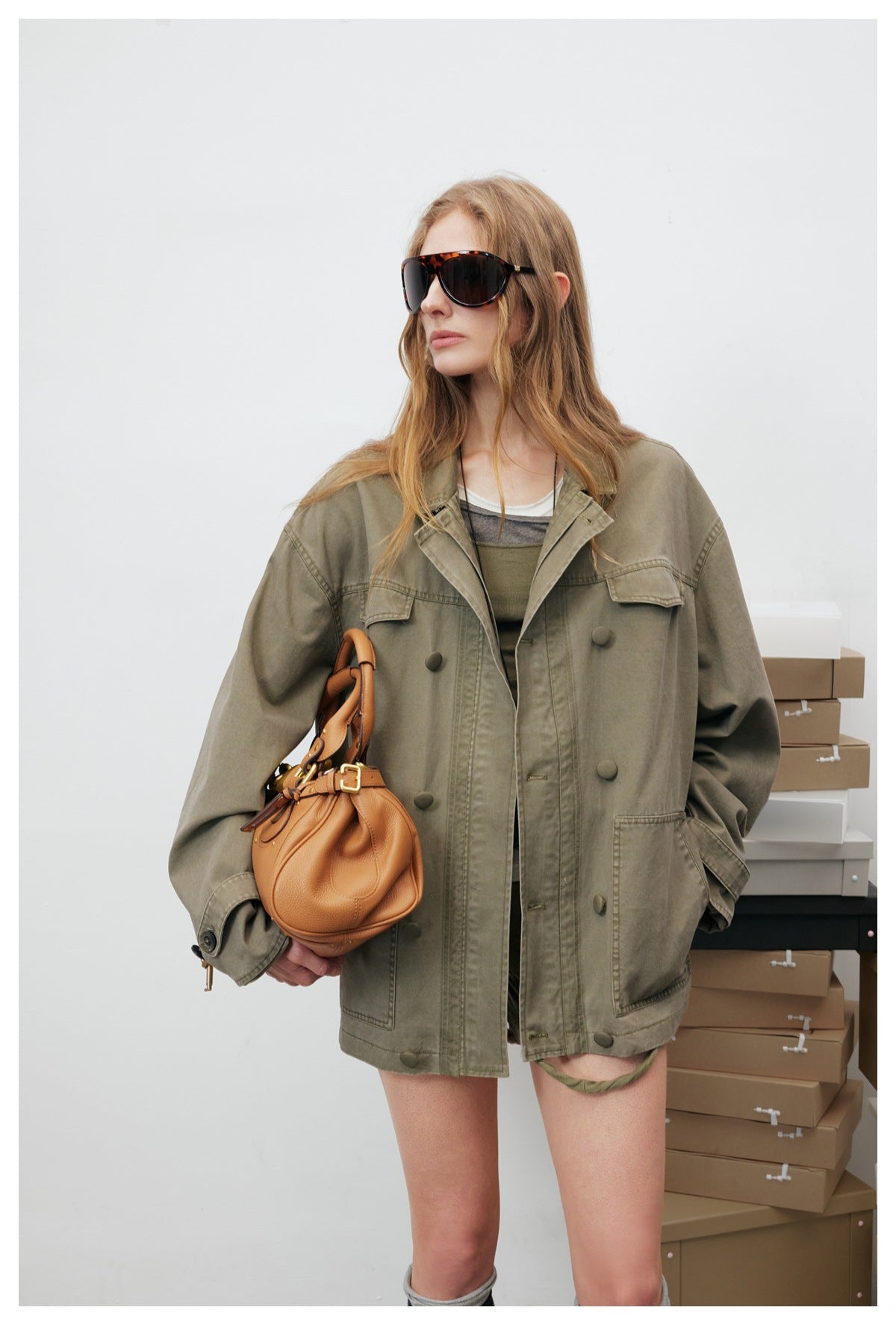 Model wearing an oversized olive utility jacket with flap and patch pockets, layered over a top; close three-quarter view.