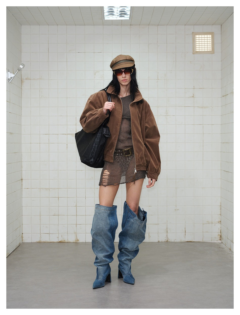 Front view of a model in a brown zip-front jacket, dark distressed skirt, blue denim boots, cap and sunglasses.