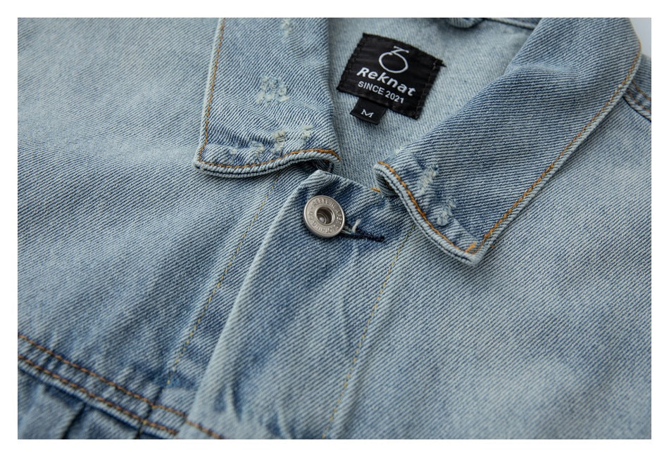 Close-up of a light blue denim jacket collar and button, with a sewn black neck label.