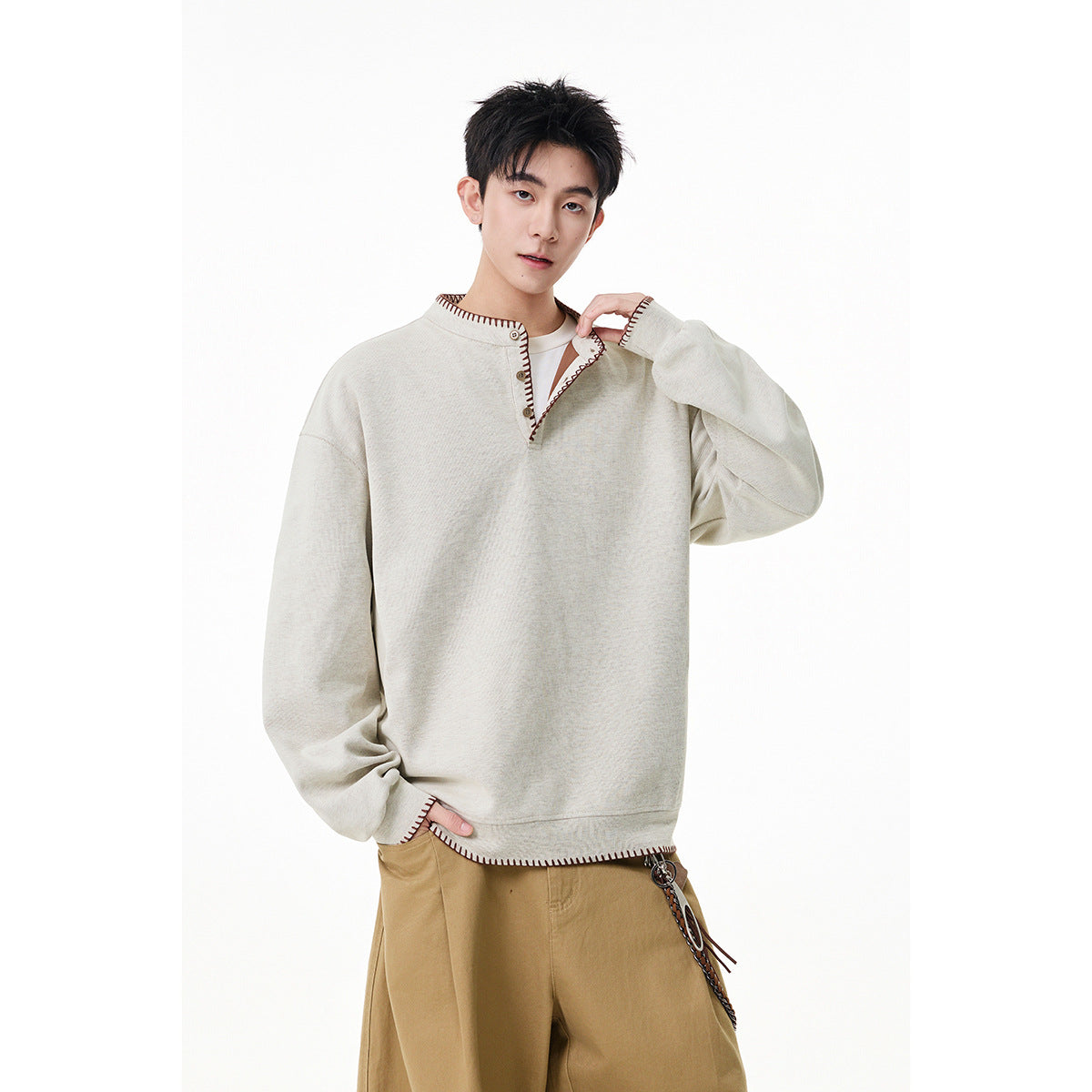 Man wearing an oversized cream pullover with a short button placket and dark brown contrast stitching.
