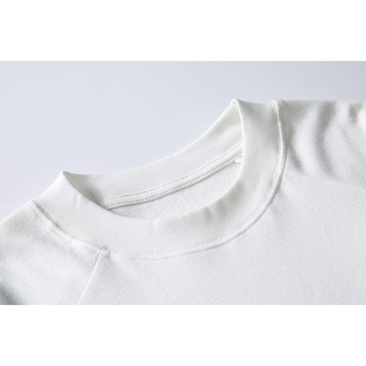Close-up of a white sweatshirt's ribbed crew neckline and shoulder seam.