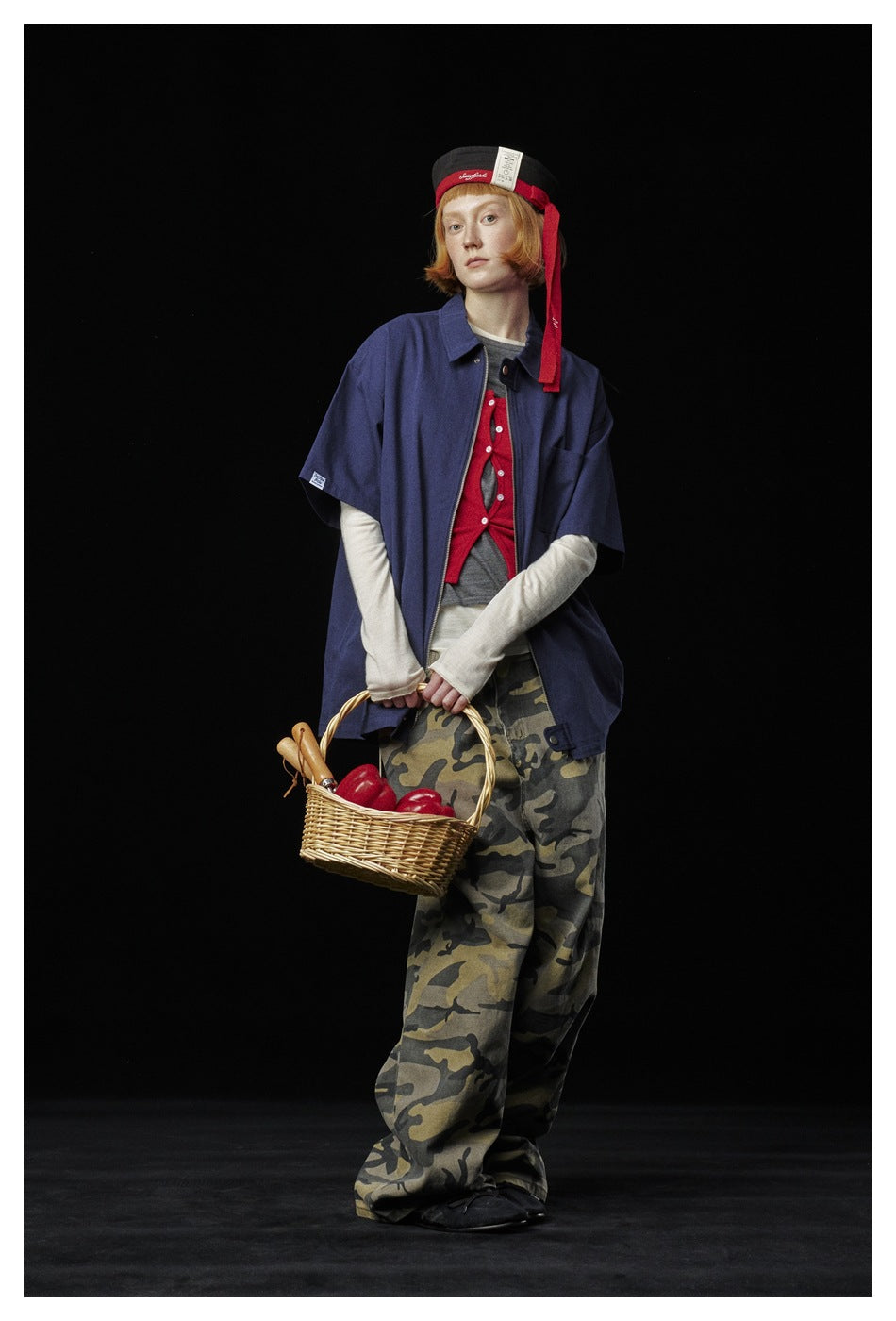 Full-length model wearing a navy short-sleeve zip shirt over layered tops and loose camouflage-print trousers.
