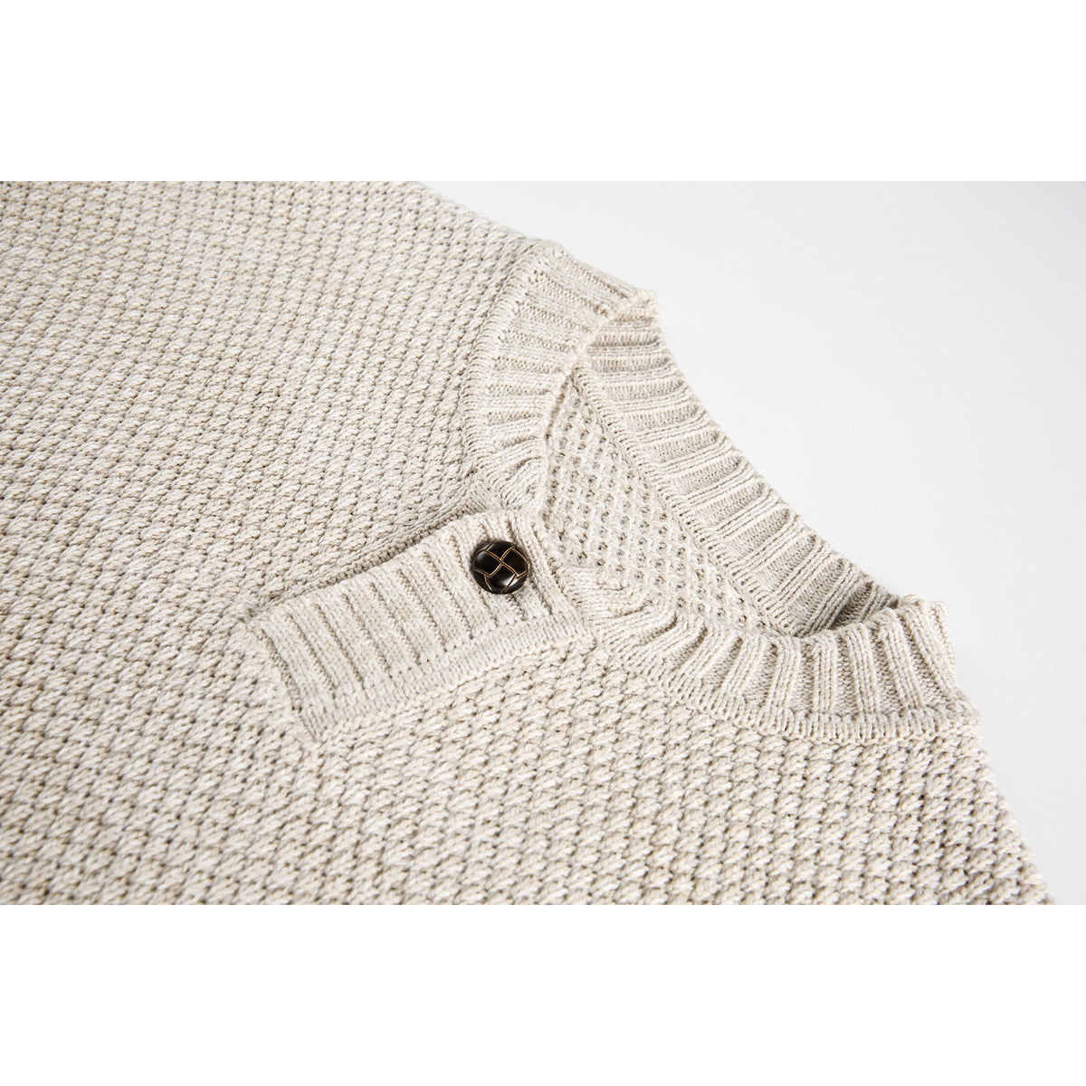 Close-up of an oatmeal knit sweater's textured fabric, ribbed neckline and single dark button.