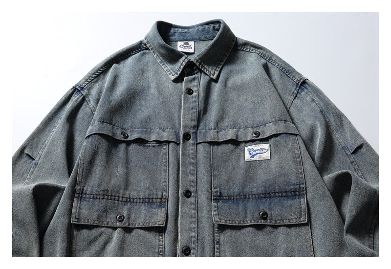 Front view of a gray washed denim shirt with black buttons, two large flap pockets and a small sewn label.