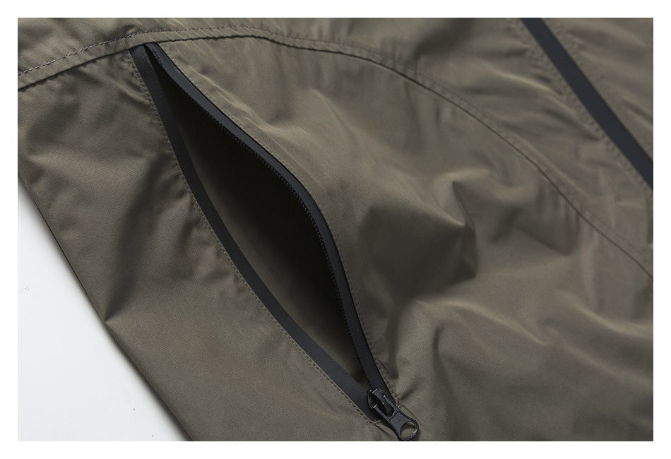 Close-up of a black water-resistant zipper pocket on gray-olive garment fabric.